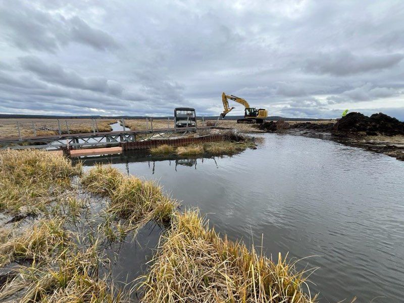 Sheet-pile structure with water on both sides and an excavator behind.